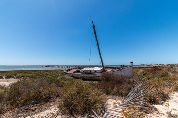 Fototapeta na wymiar Abandoned boat on the vegetation on the sand dunes of Ria Formosa marshlands located in the Algarve, Portugal.