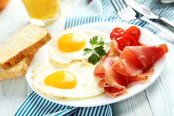 Fried eggs with bacon and toasts on plate on blue wooden table