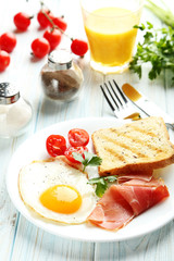 Fried eggs with bacon and toasts on plate on blue wooden table