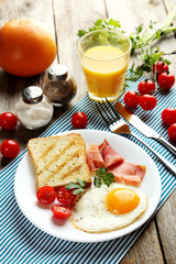 Fried eggs with bacon and toasts on plate on grey wooden table