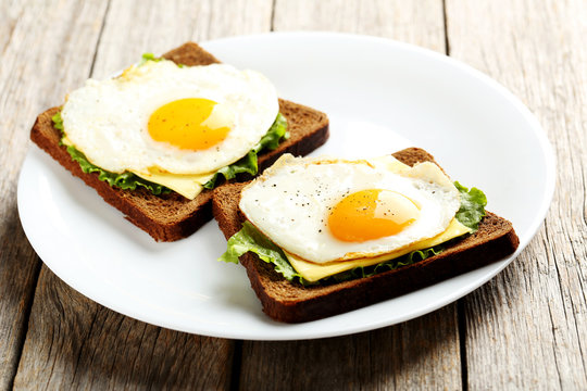 Fried eggs with toasts on plate on grey wooden table