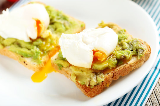 Poached eggs with avocado on toasts on grey wooden table