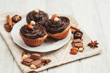 
Chocolate cupcakes with cream , almonds , hazelnuts and cinnamon on a wooden background 