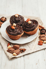 
Chocolate cupcakes with cream , almonds , hazelnuts and cinnamon on a wooden background 