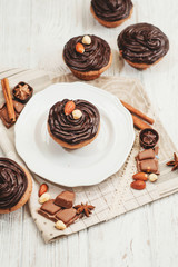 
Chocolate cupcakes with cream , almonds , hazelnuts and cinnamon on a wooden background 