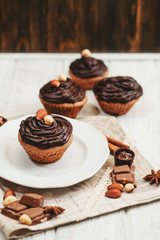 
Chocolate cupcakes with cream , almonds , hazelnuts and cinnamon on a wooden background 