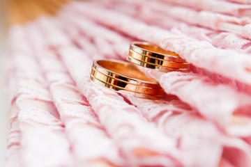 Golden wedding rings on lace pink fabric. Wedding embroidery details.