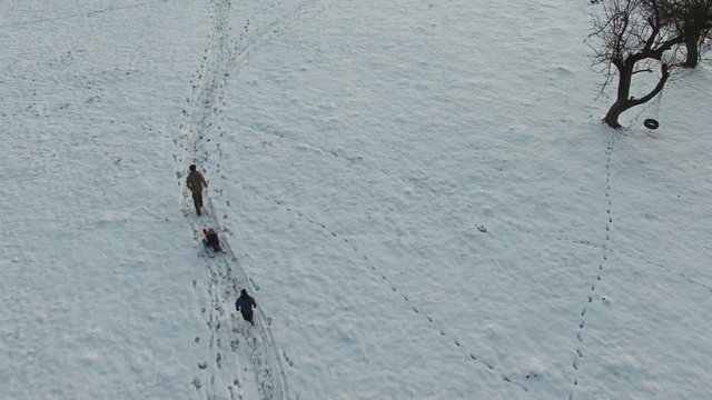 Father pulling slade and kids having fun in winter, aerial view