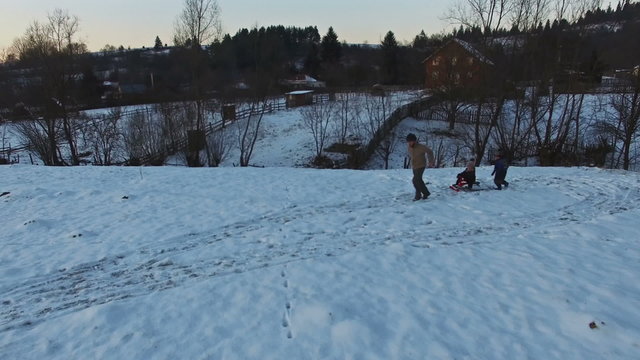 Father pulling slade with kids having fun in winter, aerial view