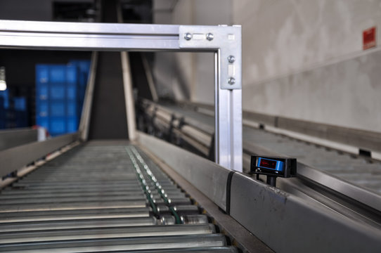 Close up shot of a roller conveyor with a laser distance sensor on the side. Photo taken in a big warehouse in Germany. Focus on the laser distance sensor.
