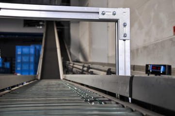 Close up shot of a roller conveyor with a ramp and a laser distance sensor on the side. Photo taken in a big warehouse in Germany. Focus on the aluminium beam.