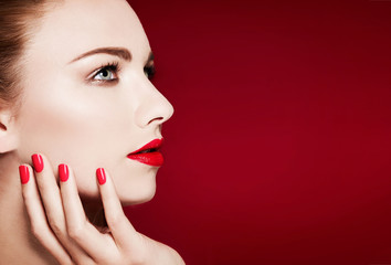 Beautiful model profile closeup beauty shot with red manicured nails and lips. Isolated on red background. 