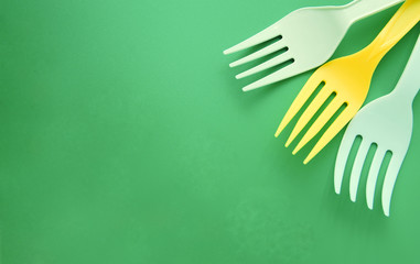 White and yellow plastic forks arranged in a corner of a green background