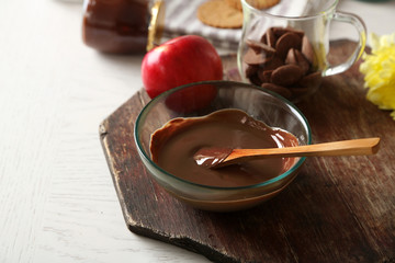 Melted chocolate in glass bowl, on wooden background