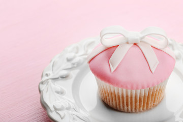 Tasty cupcake with bow on color wooden background