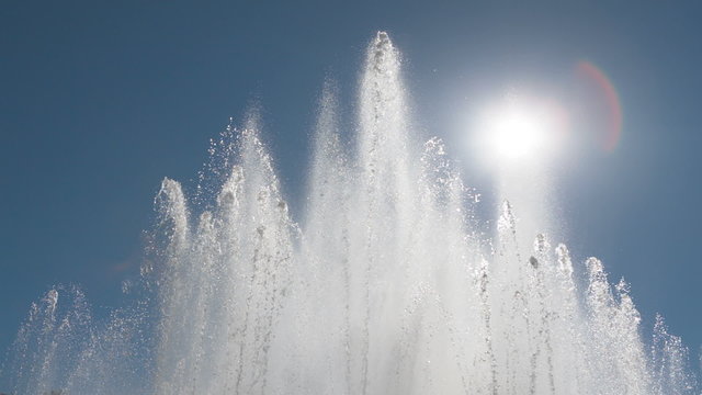 Streams of water from a big fountain with the sun and the sky as background.