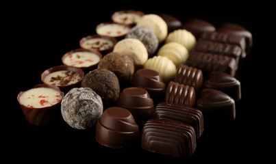 Assorted chocolate candies on black background, close up
