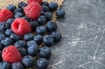 Blueberries and raspberries scattered on a jute cloth and chalkboard background, space for text
