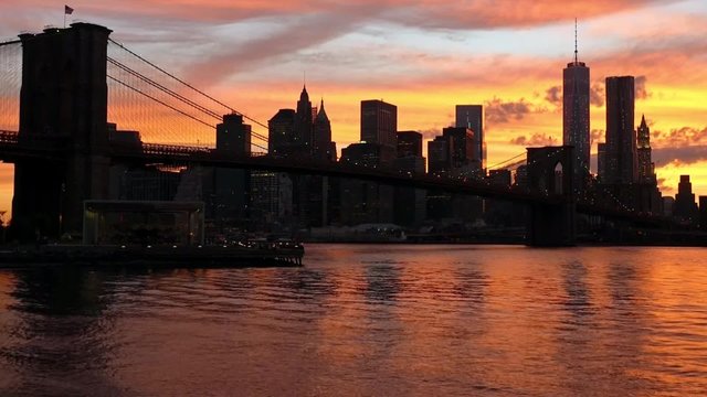 The Brooklyn Bridge and silhouette of Manhattan Island during sunset.