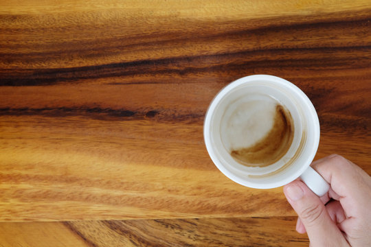 Hand holding a cup with coffee stain cup on wood background