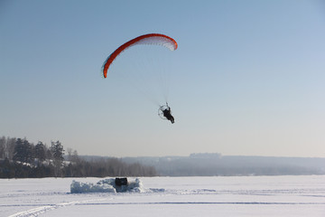 The person flying on a motorized paraplane against the snow 
