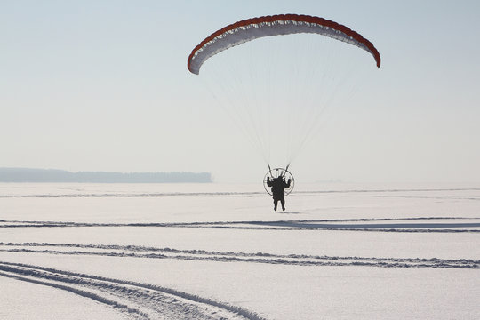 The person flying on a motorized paraplane against the snow 
