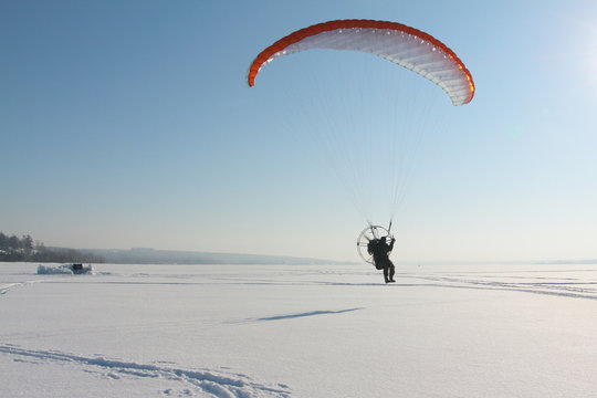 The person flying on a motorized paraplane against the snow 
