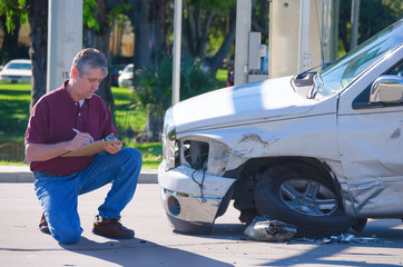 Male auto insurance adjuster inspecting a vehicle that has been in an accident wreck