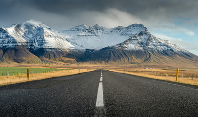 Fototapeta premium Perspektywiczna droga z śnieżnym pasma górskiego tłem w chmurnym dnia jesieni sezonie Iceland