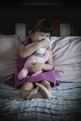 Little sad asian girl sitting on bed. Vignette picture style.