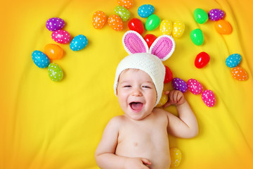 Baby boy in bunny hat lying on yellow blanket with easter eggs