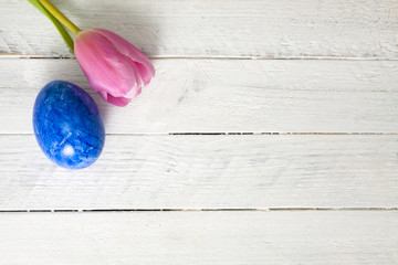 Blue easter egg with pink tulip on white wooden table, on bottom right copy space
