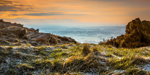 Warm glow of sunrise shining on rugged rocks before clearing the mist across the miles of low land