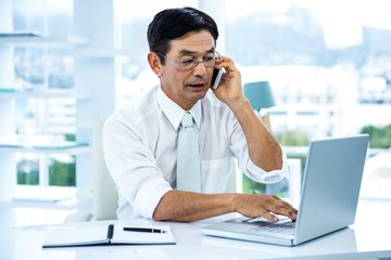 Busy asian businessman working on laptop and calling in office