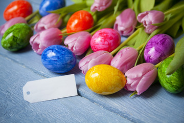 Easter eggs with tulips on blue wooden table, with empty message card