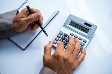 Businessman using calculator and taking notes 