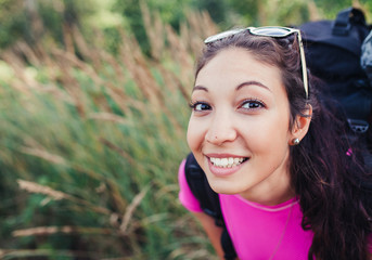 Tourist young woman with backpack walking among high grass in su