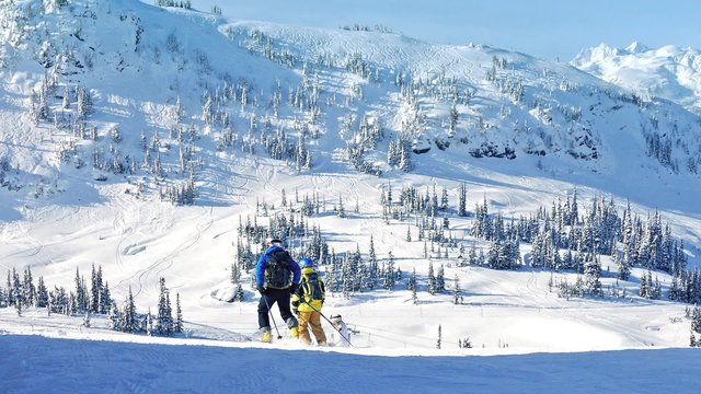 People Ski Past Mountains In The Sun