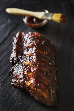 half rack of barbecued baby back ribs with sauce on slate