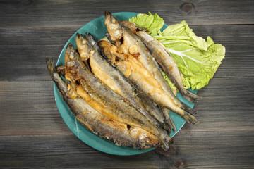 Grilled fish - smelt on a plate with green salad on an old black wooden background