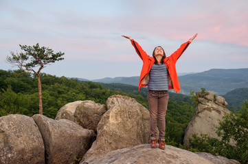 hiker standing with her arms up on big rock on top of the mounta