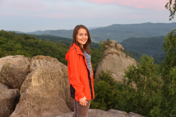Portrait of young happy girl hiker standing on rock on top of th