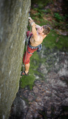 athletic man rock-climbing on large boulders with rope engaged