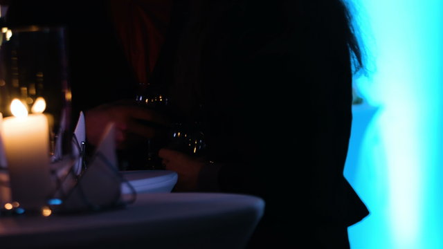 Footage of two persons in a shadow holding wineglasses near table at nightclub. 