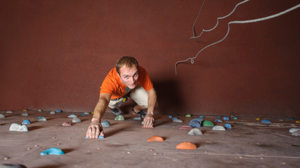 Young man climbing on practical wall in gym, bouldering indoors