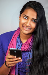 Junge Inderin mit Smartphone l&auml;chelt gl&uuml;cklich in die Kamera  