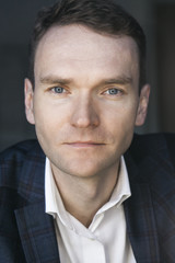 portrait of a white man in blue jacket and white shirt looking straight into the camera bright eyes serious expression blue eyes