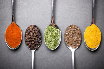 Different spices on metal spoons background.