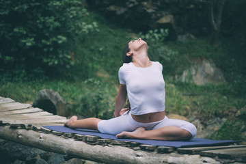 Beautiful young woman meditating in yoga pose at a mountain stream. Selective focus on woman.