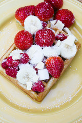 Waffle with strawberries, raspberries, sliced banana and powdered sugar
